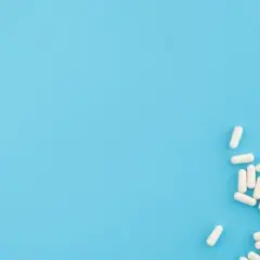 Białe kapsułki, jakby wysypane z opakowania **zahron**, leżą na jasnoniebieskim tle.