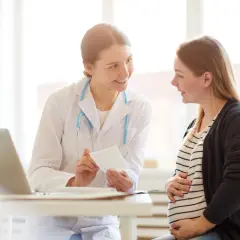 Lekarka w białym fartuchu pokazuje zdjęcie USG uśmiechniętej ciężarnej pacjentce.