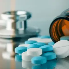 Stetoskop i butelka leków, z których wysypały się białe i niebieskie tabletki, w tym arypiprazol.