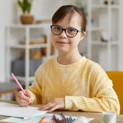 Dziewczynka z trisomią 21, w okularach, rysuje kredką.