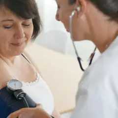 Lekarka mierzy ciśnienie pacjentce za pomocą ciśnieniomierza. Pacjentka ma na sobie białą koszulkę.
