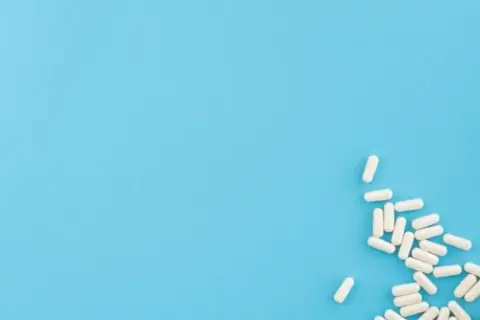 Białe kapsułki, jakby wysypane z opakowania **zahron**, leżą na jasnoniebieskim tle.