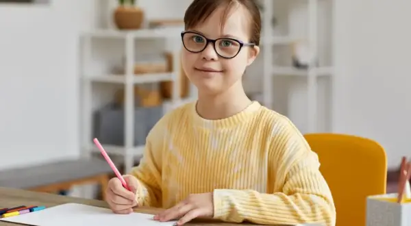 Dziewczynka z trisomią 21, w okularach, rysuje kredką.