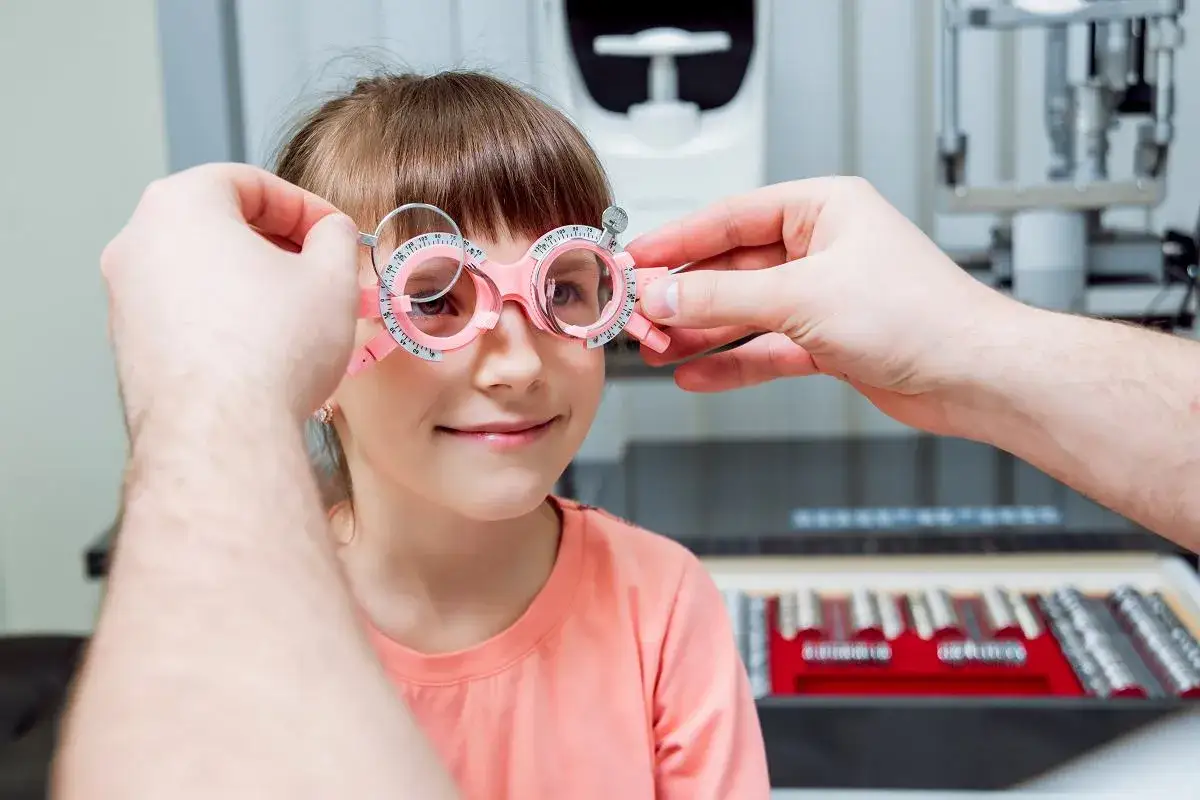 Mała dziewczynka ma badane oczy pod kątem krótkowzroczności. Okulista dopasowuje jej różowe okulary próbne.