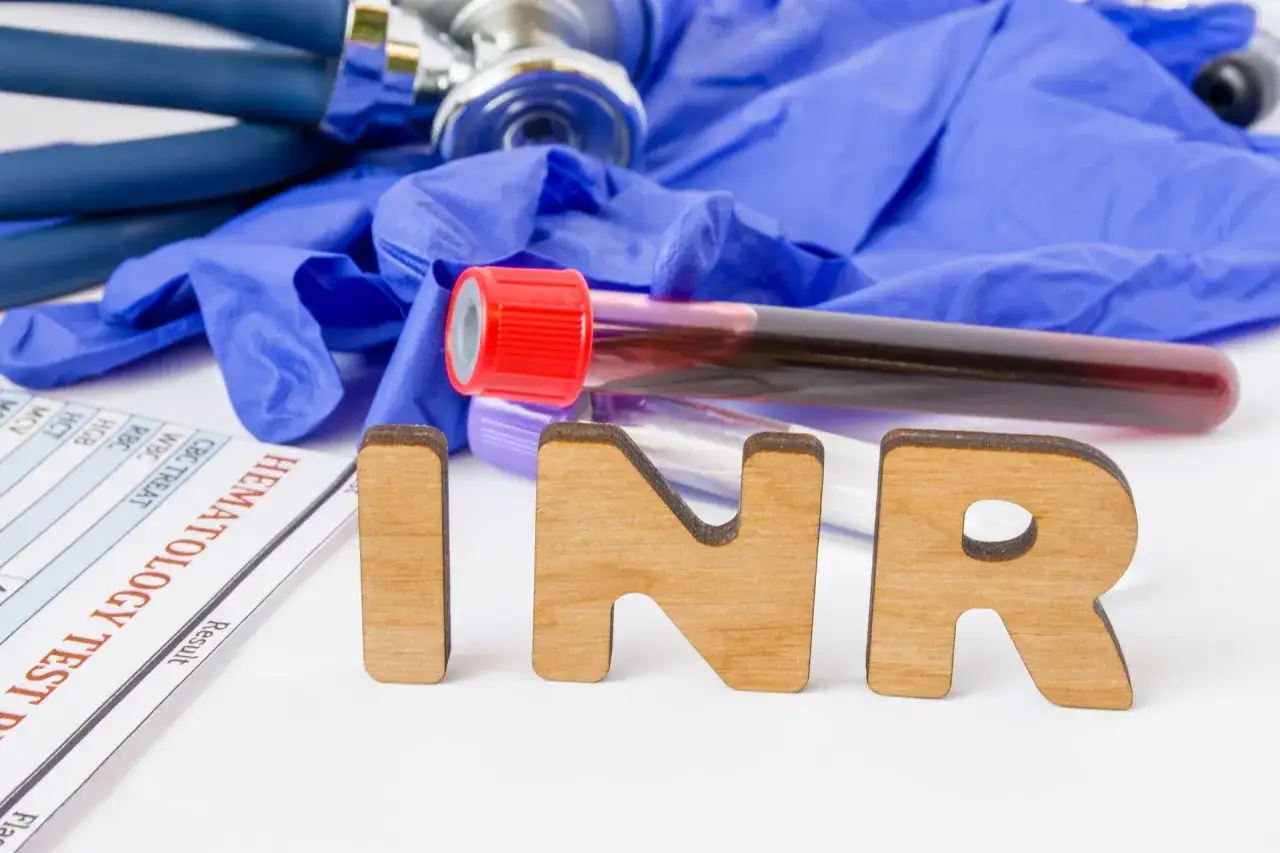 Wyniki badań hematologicznych, probówki z krwią, rękawiczki i stetoskop. Litery INR wskazują na badanie czasu protrombinowego.