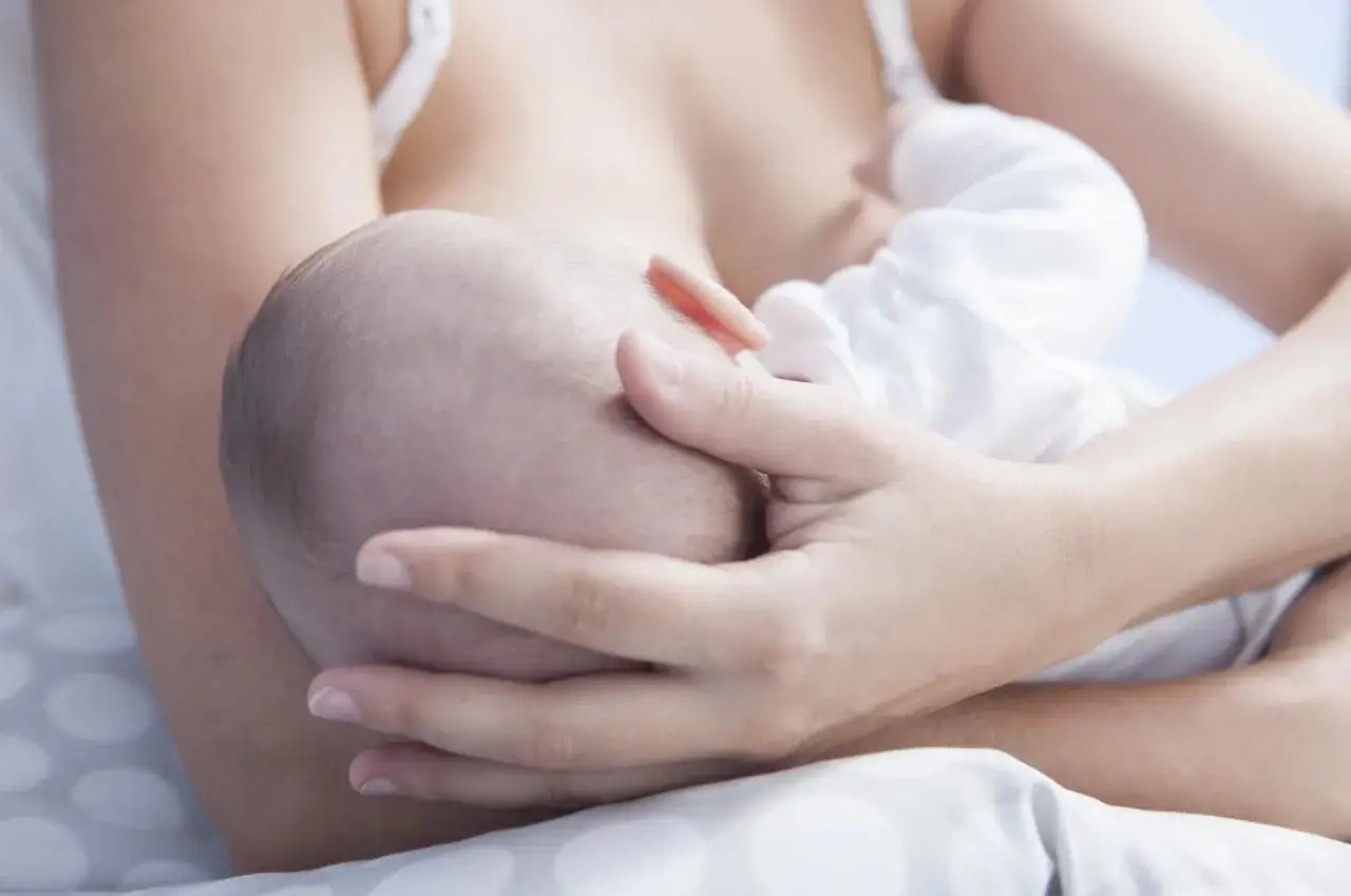 Matka karmi piersią dziecko. Delikatne dłonie otulają główkę maluszka. To piękny moment bliskości, choć czasem może pojawić się zapalenie piersi.