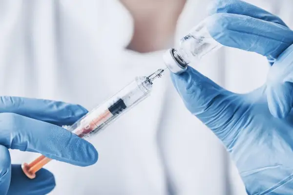 Ręce w niebieskich rękawiczkach przygotowują zastrzyk z biofuroksymem, pobierając płyn ze szklanej fiolki do strzykawki.